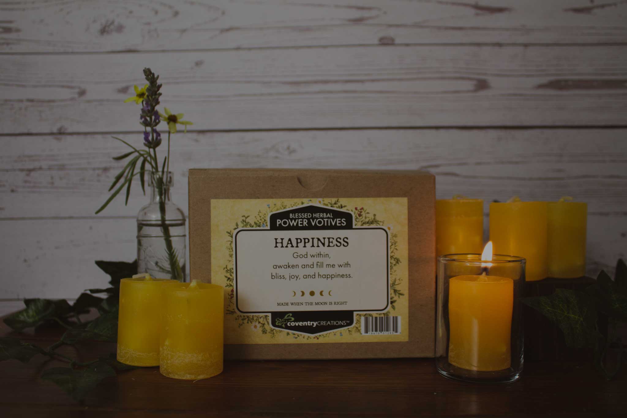 Box of Blessed Herbal Yellow Happiness Power Votive Candles with one lit