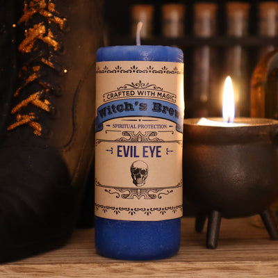 Coventry Creations Witch’s Brew Evil Eye Brilliant Blue Candle with candle lit and witch shoe behind